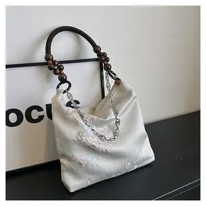 Detail of silk floral embroidery on off-white tote bag with wooden bead handle