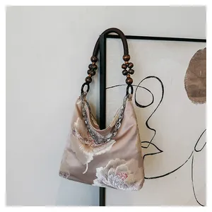 Detail of silk tote bag featuring floral embroidery, wooden beads, and silver chain