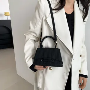 Vue détaillée du sac carré noir texturé avec sangle décorative sur blazer blanc