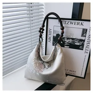 Detail of floral embroidery on beige silk tote bag with wooden bead and metal chain