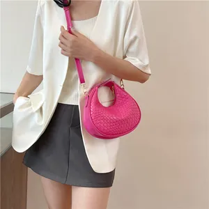 Detail of hot pink crescent bag with woven leather texture and metal hardware on model