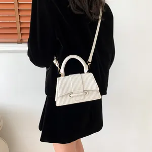 Détail du sac bandoulière blanc texturé avec côtes verticales sur un costume en velours