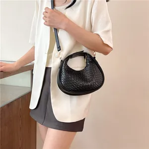 Close-up of black woven crescent bag with gold hardware worn by model in white blazer