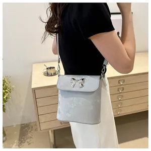 Detalle de bolso bandolera plateado con hebilla de lazo metálico en una modelo