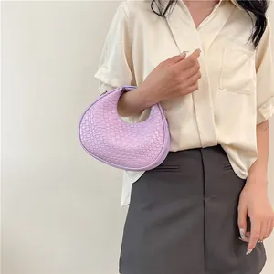 Detail of light purple woven crescent handbag held by model in elegant attire