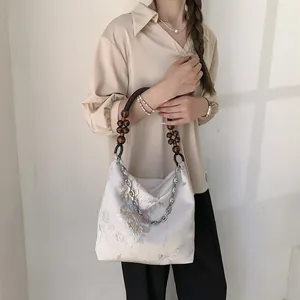 Elegant beige silk tote bag with floral embroidery and dark wooden bead handle detail