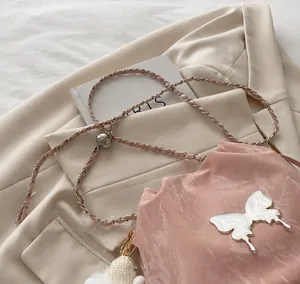 Detalle de correa de hombro en cuero rosa con cadena y hebilla de mariposa blanca