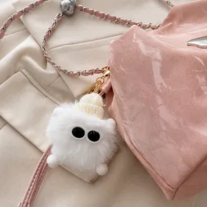 Detalle de llavero de monstruo de peluche blanco con gorro sobre bolso plisado rosa