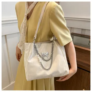 Detalle del bolso crema con dije de mariposa plateada y decoración de cadena de perlas