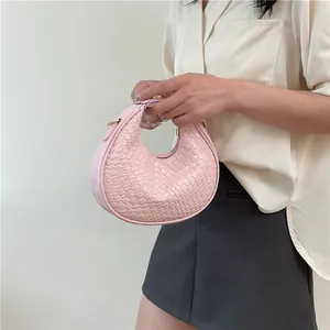 Close-up of pink woven crescent bag featuring golden hardware held by a model