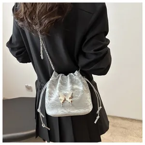 Detail view of silver drawstring bucket bag with metallic texture and butterfly ornament