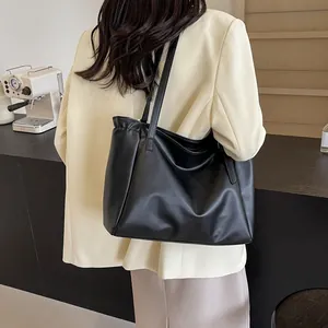 Détail d'un grand sac cabas noir en cuir PU porté avec un blazer beige classique