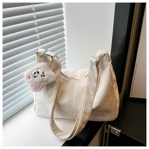 Close-up of beige tote bag texture with pink plush monster charm and adjustable strap