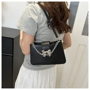 Detail of black crossbody bag with silver chain strap and metal bow clasp on a model