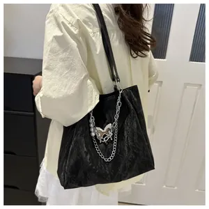 Detalle del bolso tote plisado negro con cadena plateada, perlas y colgante de mariposa chic