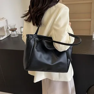Détail d'un sac cabas minimaliste en cuir noir avec de fines bretelles sur l'épaule