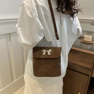 Bolso bandolera de ante marrón con lazo plateado en un ambiente moderno de casa