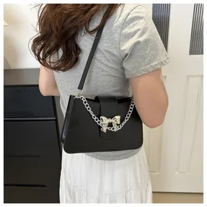 Detail of black leather shoulder bag with silver bow buckle and decorative chain