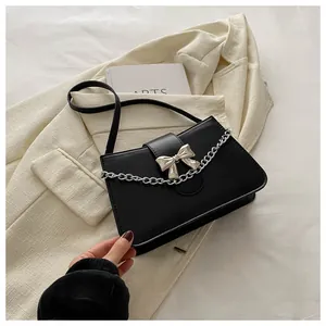 Detail view of black crossbody bag featuring silver bow accent and fine chain strap