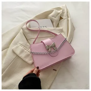 Detail of pink crossbody bag with silver bow accent and chain on a beige blazer