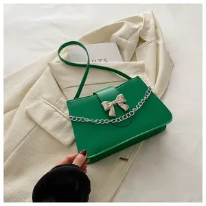 Detail of green square crossbody bag with silver bow and chain on beige background