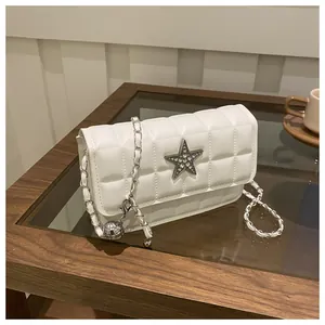Detail of white quilted crossbody bag with sparkling star emblem and silver chain strap