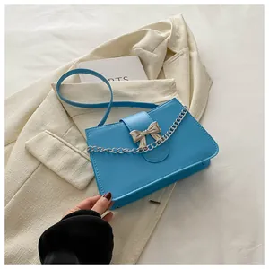 Close-up of bright blue crossbody bag with silver bow buckle and chain detail