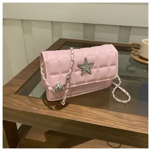Pink quilted crossbody bag detail with silver star buckle and chain strap on a table