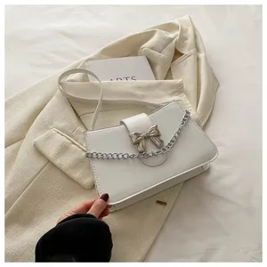 Close-up of a white minimalist crossbody bag with a silver bow lock and chain detail