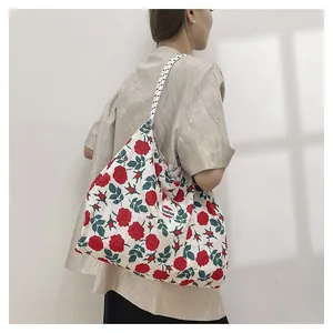 Floral canvas tote bag with red roses and woven straps shown from a side-view on a shoulder