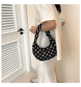 Detail of checkered canvas hobo bag with fringe edges on a minimalist indoor background