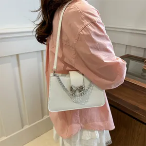 Elegant white crossbody bag with silver chain and bow buckle on model in pink shirt