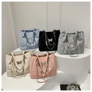 Detalle de cinco bolsos plisados con colgantes de mariposa metálica y cadenas de perlas