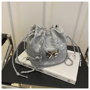 Detailed view of silver drawstring bucket bag with metallic butterfly and chain strap