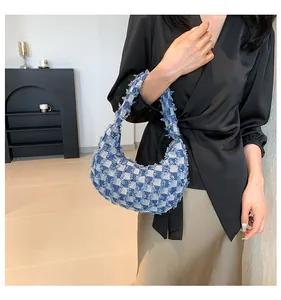 Close-up of blue checkerboard denim crescent bag featuring distressed fringe details