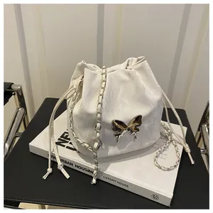 Close-up of white drawstring bucket bag with silver butterfly charm and chain strap