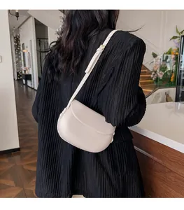 Détail d'un sac besace en cuir crème avec rabat incurvé et finitions de rivets élégants