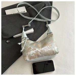 Gros plan d'un sac à bandoulière bleu céladon avec broderie en brocart doré et satin