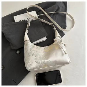 Détail de broderie chinoise sur sac en satin avec bandoulière en cuir blanc
