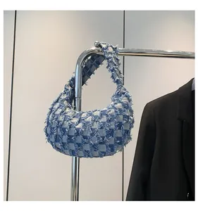 Detail of blue denim checkerboard shoulder bag with frayed edges hanging on a metal hanger