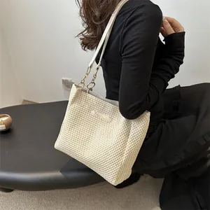 Detalle de un bolso tote de punto beige con cadena dorada y etiqueta de moda