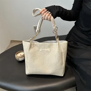 Vista detallada del bolso de paja con correa de cadena y logo metálico de moda