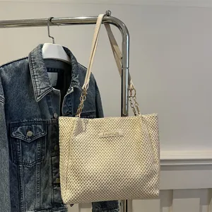 Detalle de bolso tote de paja beige con etiqueta Fashion y correa de cadena en percha