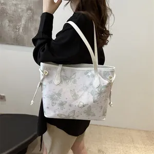 Détail d'un cabas blanc avec motif papillon vert et garnitures dorées porté par un modèle