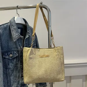 Detalle del bolso de paja con tejido beige, correa marrón y cadena de metal dorado