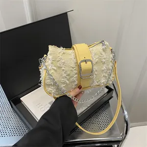 Detail of light yellow woven crossbody bag with fringe texture and silver chain strap