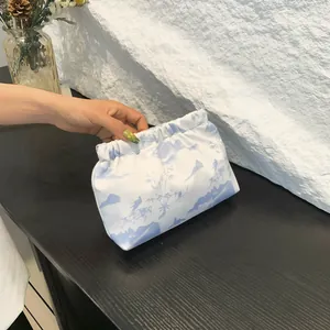 Pochette plissée élégante avec imprimé floral bleu tenue devant un mur décoratif