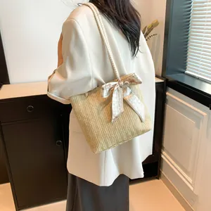 Detailed close-up of woven straw tote bag with white rope strap and bow decoration