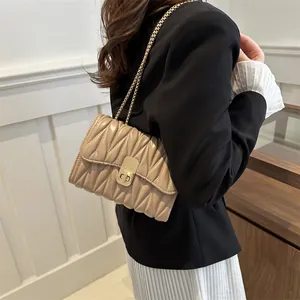 Détail du sac matelassé beige avec chaîne dorée porté par un mannequin en costume