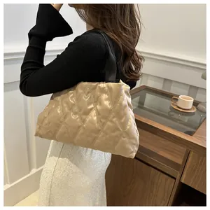 Chic quilted tote bag with black webbing handle worn by a model in a cozy indoor setting